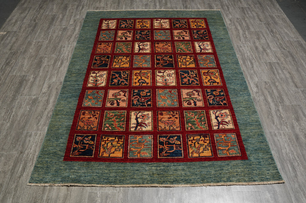 A rectangular area rug with a teal-green textured border and a central grid of small square panels in red, orange, beige, and navy, laid out on a gray wood-look floor.