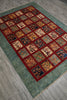 Load image into Gallery viewer, A rectangular area rug with a teal-green textured border and a central grid of square panels in red, orange, beige, and navy, shown laid out on a gray wood-look floor.