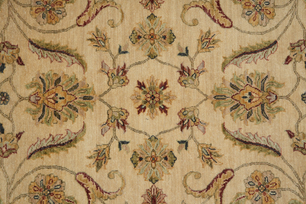 A close-up of a woven textile or rug pattern with a beige background and ornate floral motifs in muted green, rust red, mustard yellow, and brown.