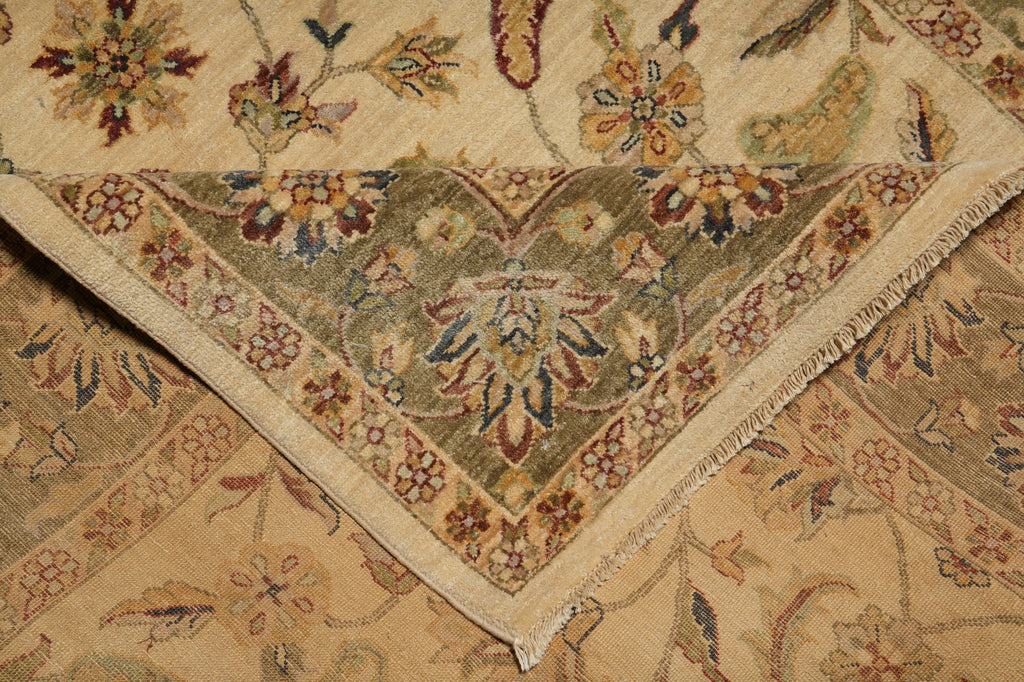 A close-up of a traditional patterned rug showing the corner and fringe detail, with a beige base and floral motifs in muted green, brown, and red.