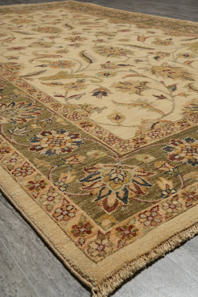 A traditional oriental area rug with a beige and olive green base, featuring floral motifs and a detailed border, laid out on a gray wood floor.
