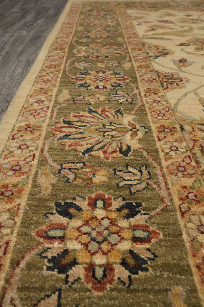 A close-up view of a traditional oriental-style runner rug with a beige and olive green base, featuring intricate floral motifs in red, blue, and yellow.