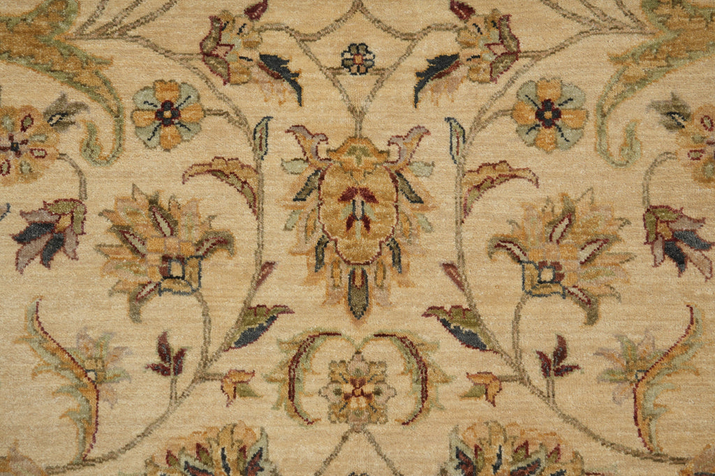 Close-up of an ornate floral rug pattern in warm beige, tan, muted green, and brown tones, showing detailed woven texture and symmetrical botanical motifs.