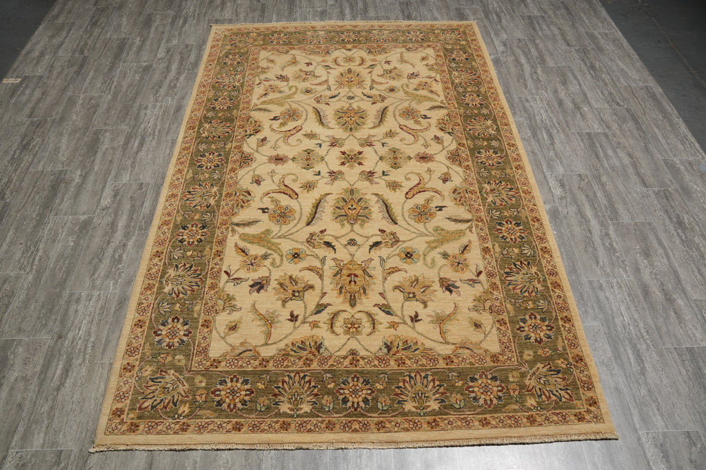 A rectangular traditional area rug with an ornate floral and vine pattern, laid flat on a gray wood-look floor. The rug features a warm beige center, a dark olive green inner border, and a light tan outer border with multicolored floral motifs.