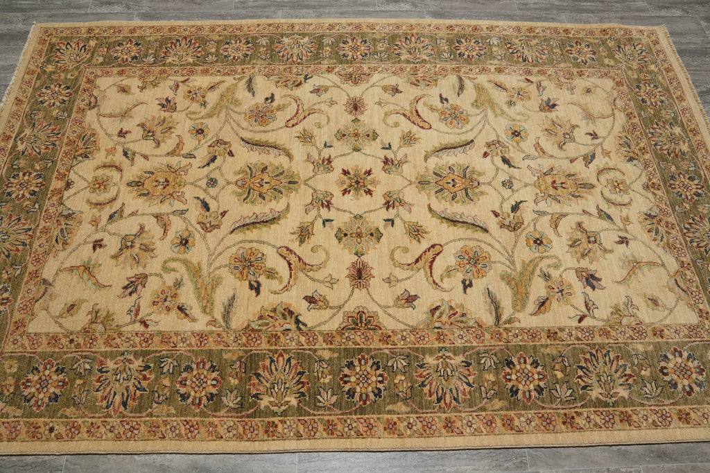 An ornate rectangular area rug with a traditional floral and vine pattern, featuring a cream center field and a detailed olive green border, laid out on a gray tiled floor.