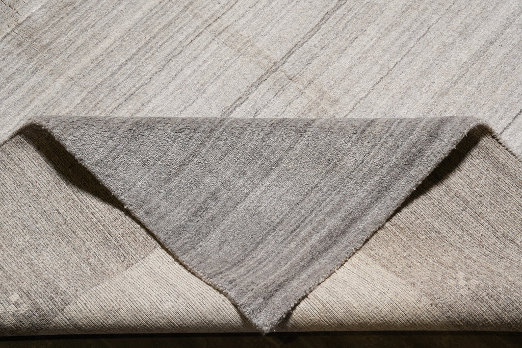 A close-up of a folded area rug showing its textured, heathered gray and beige woven pattern.