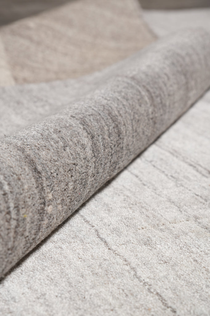 Close-up of a light gray wool felt rug with a rolled section showing the dense, textured pile.