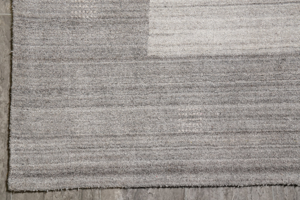 Close-up of a gray textured rug with a subtle geometric block pattern, laid on a gray wooden floor.