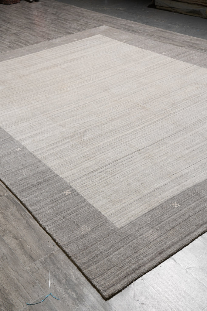 A rectangular area rug with a wide light beige center and a contrasting medium gray border, shown laid out on a gray wood-look floor.