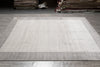 Load image into Gallery viewer, A large rectangular area rug with a light beige center and a medium gray border, laid out on a gray tiled floor in what appears to be a showroom or warehouse.
