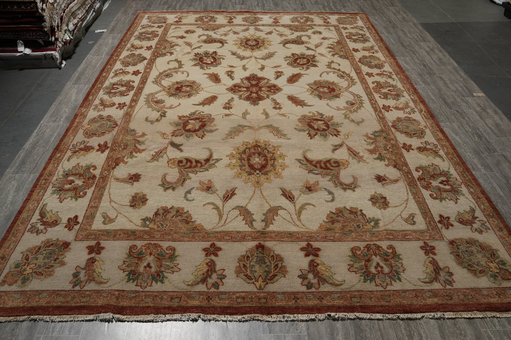 An oriental area rug with a traditional floral and medallion pattern, featuring a cream background with rust red, gold, and green accents, laid out on a gray wood floor.