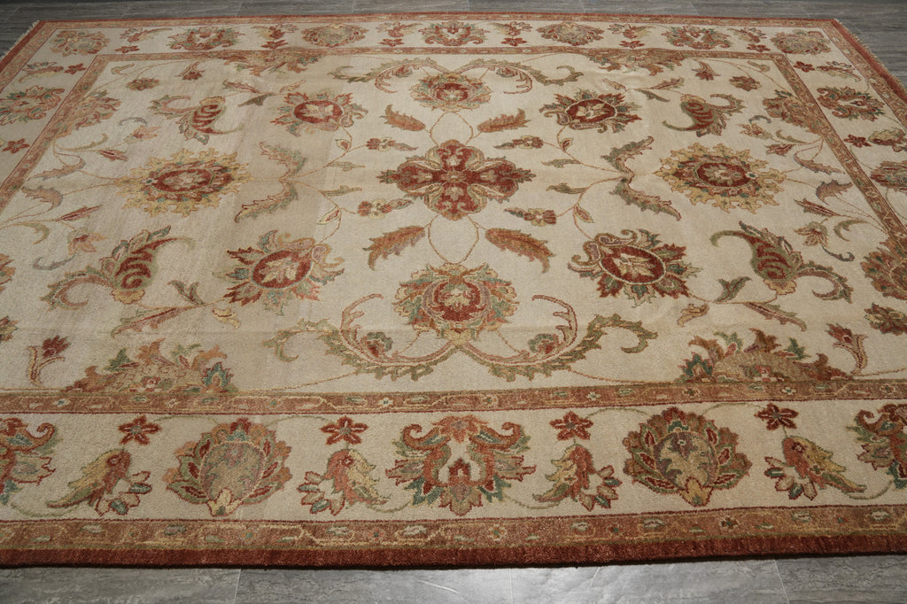 An ornate traditional area rug with a cream background and intricate floral motifs in rust red, olive green, and tan, laid out on a gray tiled floor.
