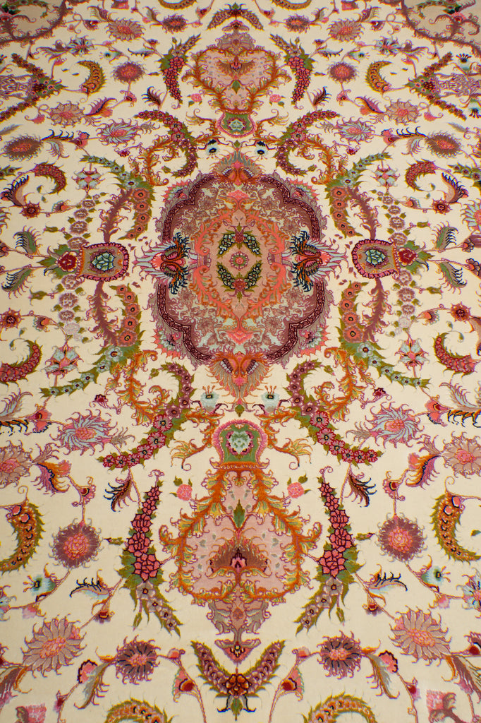 Detailed pattern view of the Persian Tabriz rug's central medallion with symmetrical floral and paisley design in coral, purple, and green on an ivory ground