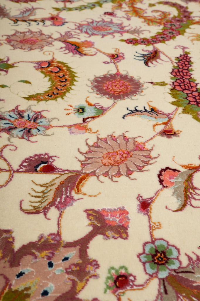 Close-up of the Persian Tabriz rug field pattern with hand-knotted floral blossoms in pink, coral, and green on an ivory background