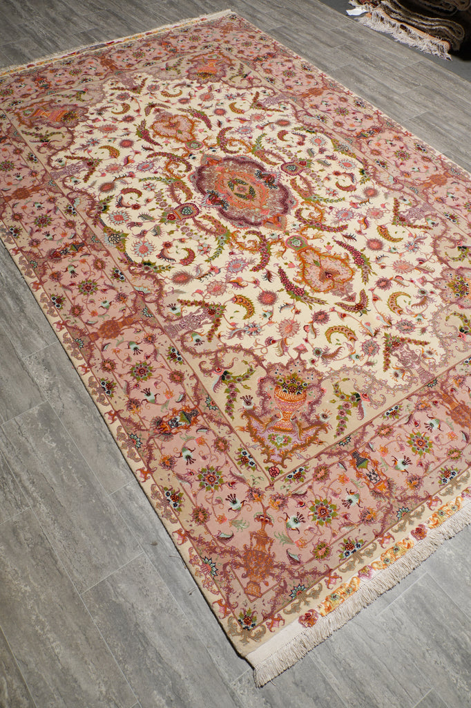 6.7 x 10.3 Persian Tabriz rug on a gray wood-look floor, showing the ivory center medallion with pink border and orange, green, and blue floral accents