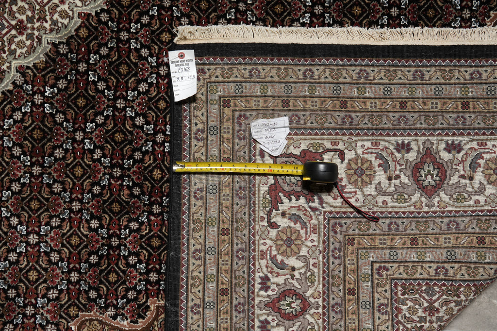 Two patterned rugs with a measuring tape between them, on a checkered floor.