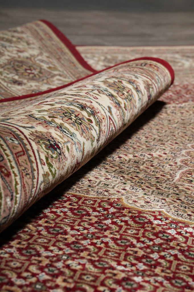 Rolling out a patterned rug with intricate designs on a wooden floor.