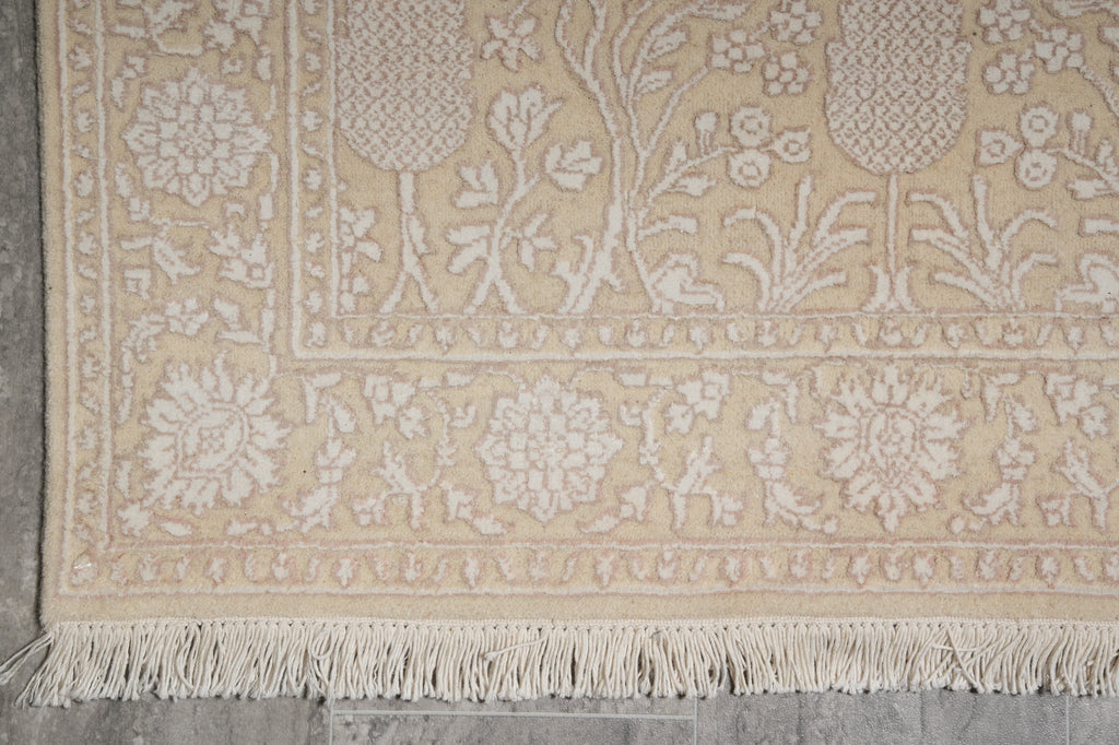 Close-up of a beige and white patterned rug with fringe on a gray floor.