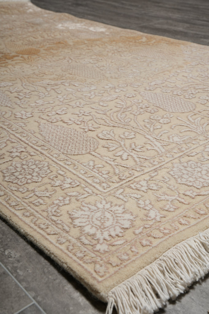 Beige patterned rug with tassels on a gray floor.