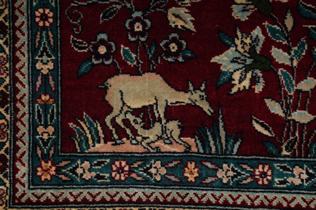 Close-up of a rug with deer and floral patterns on a dark red background