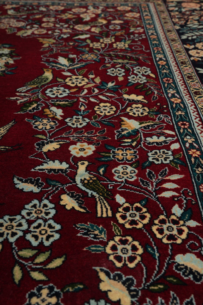 Close-up of a patterned rug with floral and bird designs on a red background.