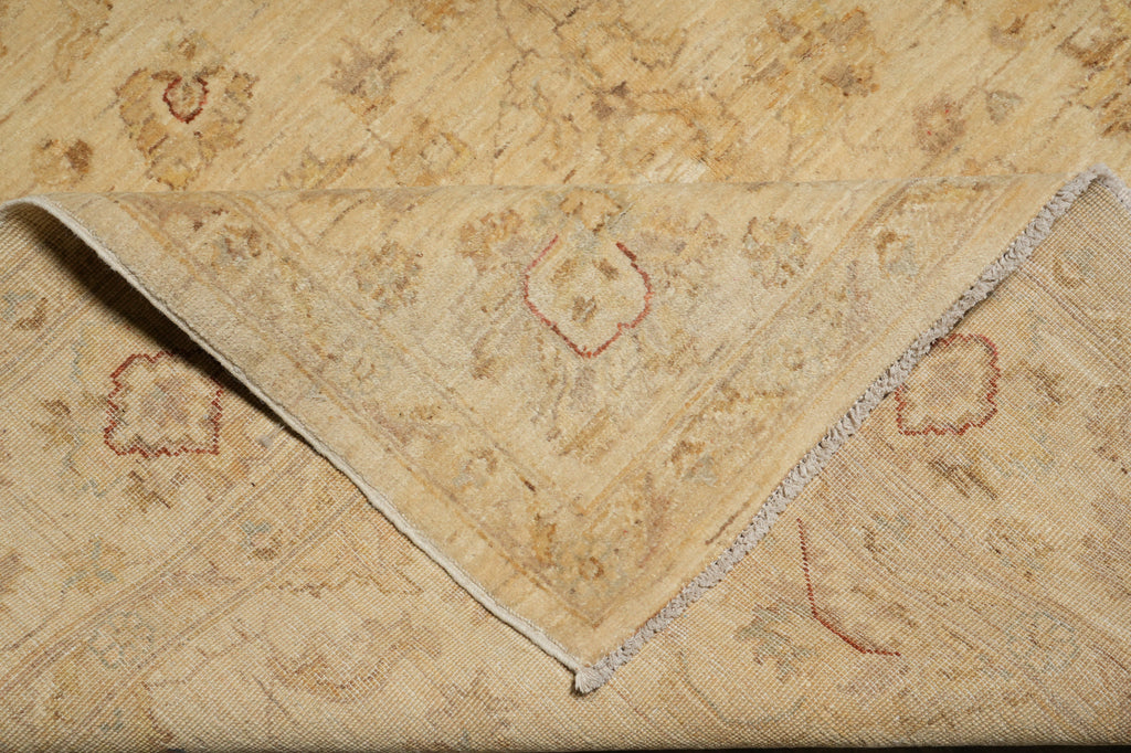 A close-up of a vintage patterned textile, likely a rug or throw blanket, featuring a beige and tan floral design with red embroidered accents and a folded corner showing a frayed edge.
