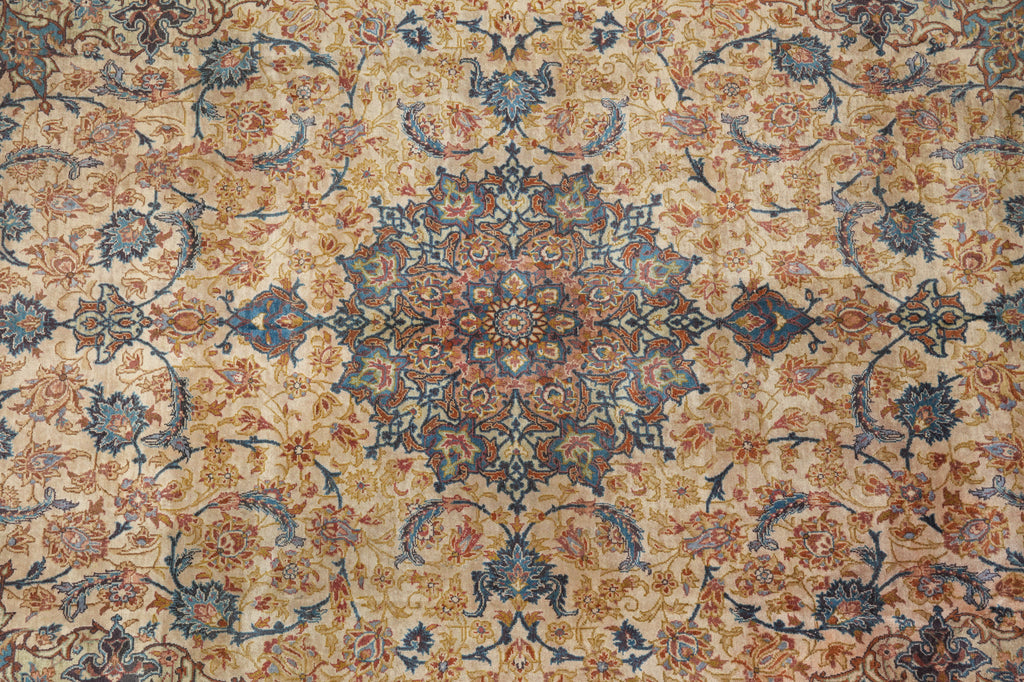 A close-up of an ornate traditional patterned rug with a central medallion and floral motifs in beige, blue, rust orange, and brown tones.