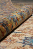 Load image into Gallery viewer, A close-up of a rolled section of a patterned area rug, showing its detailed texture and a mix of beige, blue, brown, and rust-orange colors.