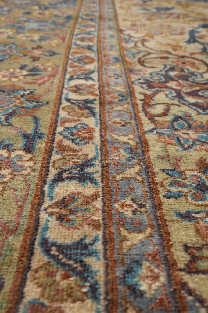 Close-up of an ornate patterned rug with beige, blue, and brown floral and scroll motifs.