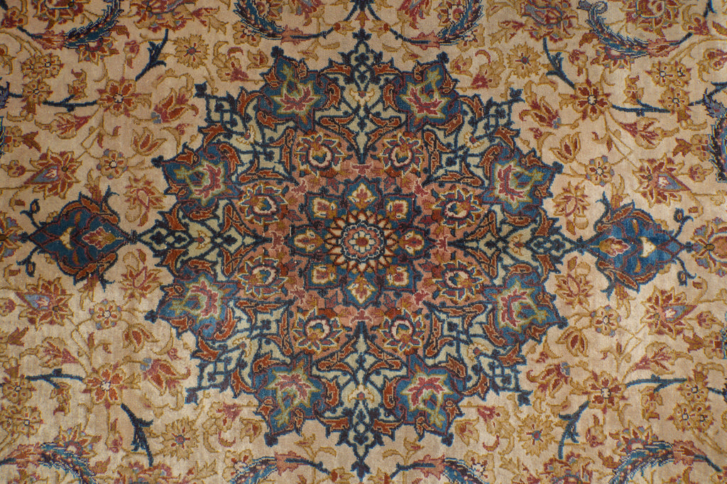 A close-up of an ornate traditional patterned rug with a central medallion and floral motifs in beige, blue, rust orange, and green.