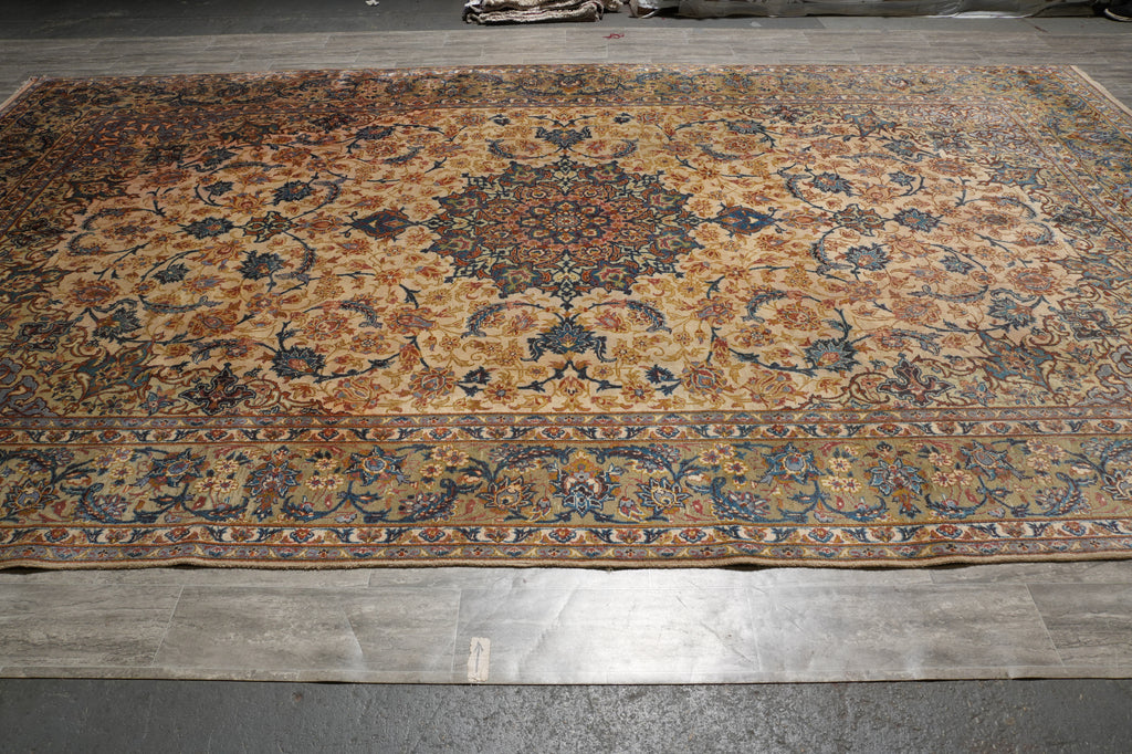 A large traditional oriental area rug with an intricate floral pattern in beige, brown, blue, and orange tones, laid out on a gray tiled floor.