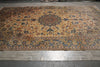 Load image into Gallery viewer, A large traditional oriental area rug with an intricate floral pattern in beige, brown, blue, and orange tones, laid out on a gray tiled floor.