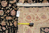 Load image into Gallery viewer, A close-up of a patterned area rug with cream, pink, and beige floral motifs on a black field, shown with a tape measure and price tag to indicate scale.