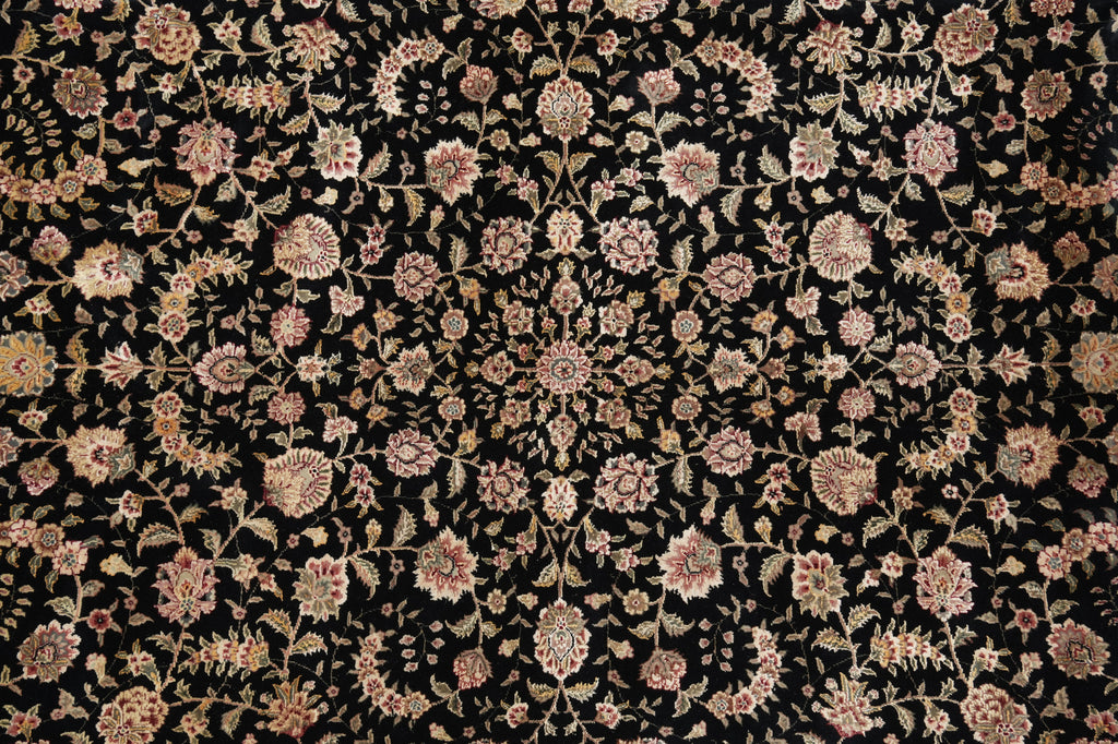 A close-up of a black fabric or rug featuring an intricate floral pattern in shades of pink, beige, and muted gold.