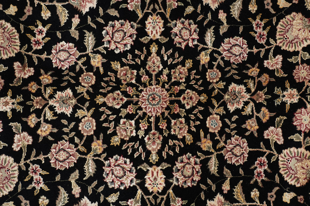 A close-up of an ornate floral rug pattern with pink, beige, and muted gold motifs on a black background.