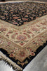 Load image into Gallery viewer, A close-up of an ornate patterned rug shown at an angle, featuring a cream and beige central field with floral motifs, a black border, and a dark navy section with dense floral patterning.