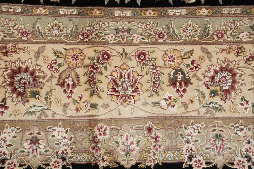 A close-up of an ornate floral patterned rug or textile with cream, beige, burgundy, green, and brown detailing, showing repeating botanical motifs and borders.