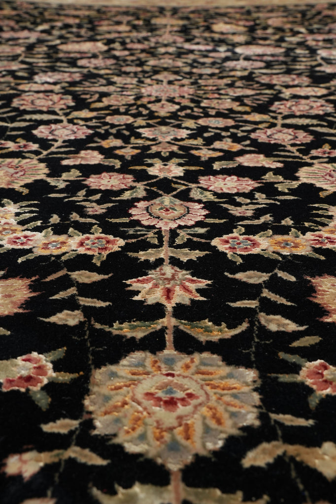A close-up of an ornate floral patterned rug with a black background and cream, pink, and muted blue motifs.