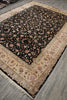Load image into Gallery viewer, A traditional oriental area rug with a black field, beige borders, and pink floral motifs, shown laid out on a gray wood floor.