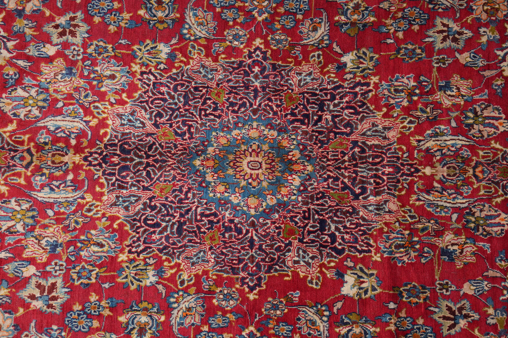 A close-up of a traditional Persian-style rug featuring a vibrant red background with a central medallion and intricate floral motifs in blue, beige, and gold.