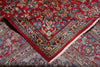 Load image into Gallery viewer, A close-up of a traditional oriental rug with a deep red field, intricate floral motifs in blue, beige, and gold, and a decorative border with white fringe.