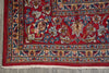 Load image into Gallery viewer, A close-up of a traditional patterned rug corner, showing a deep red field with ornate floral motifs and a detailed multi-colored border in blue, beige, and gold, finished with white fringe.