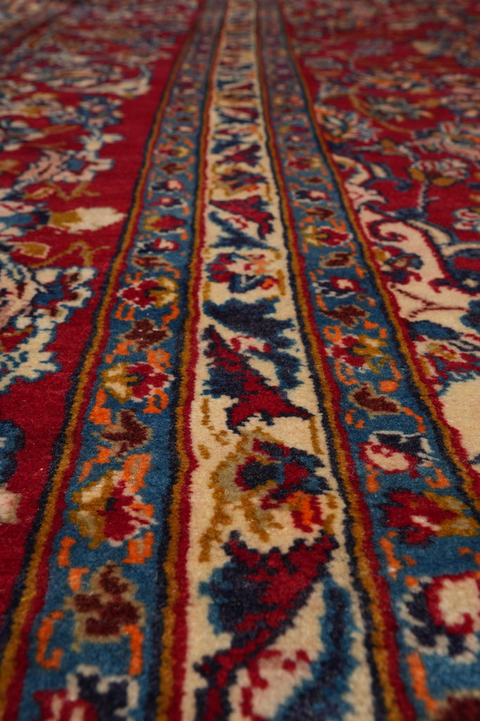 A close-up of a patterned rug showing detailed woven bands in red, blue, cream, and orange with floral motifs.