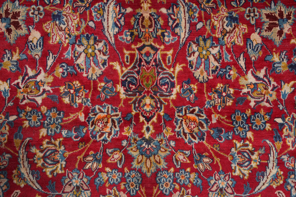 A close-up of a traditional patterned rug with a vibrant red background and intricate floral motifs in blue, beige, and gold.