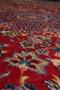 Load image into Gallery viewer, A close-up view of a traditional patterned area rug with a vibrant red field, featuring intricate floral motifs in blue, beige, and brown.