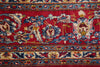 Load image into Gallery viewer, A close-up of a traditional patterned rug featuring a vibrant red field with intricate floral motifs in blue, beige, and gold, bordered by detailed floral bands.