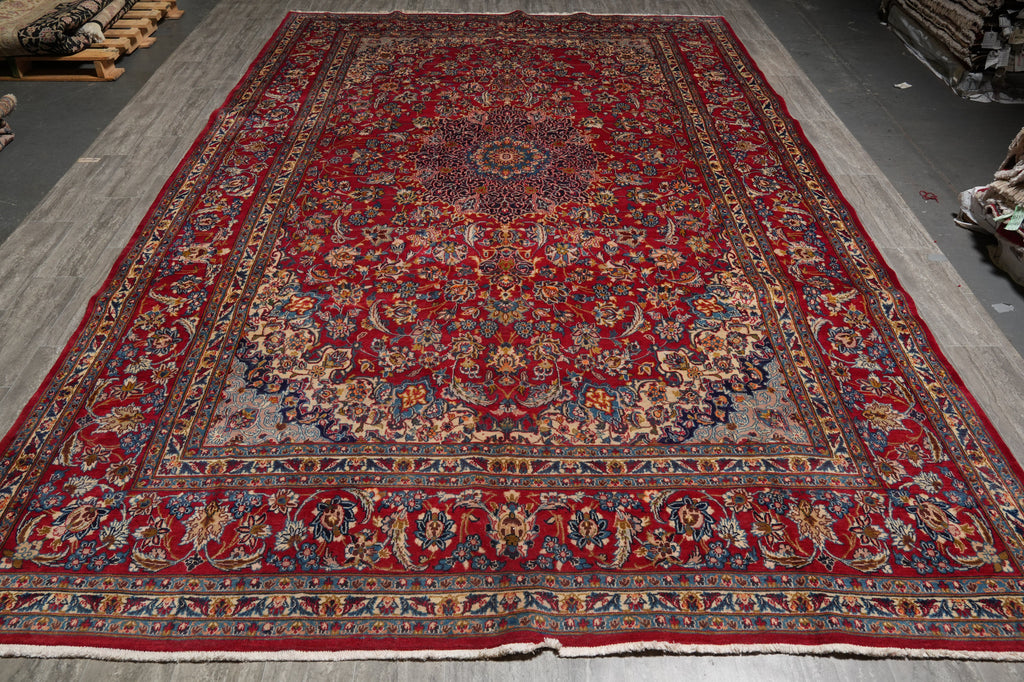 A large traditional Persian-style area rug with a deep red field, ornate floral motifs, and a detailed multi-colored border, displayed flat.