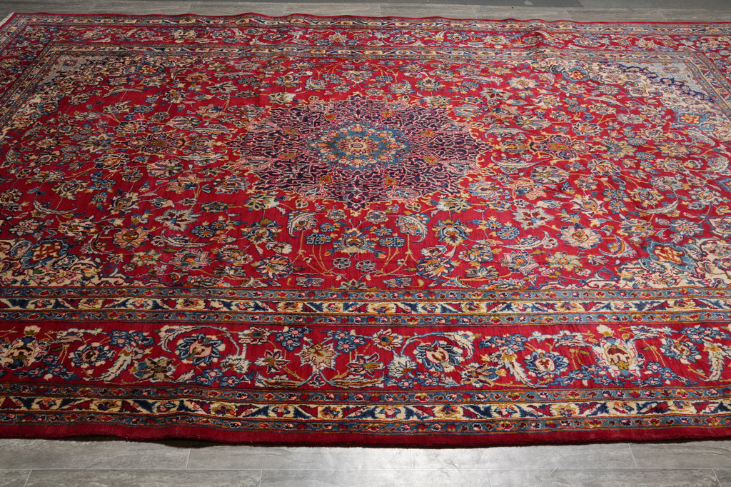A large traditional oriental area rug with a vibrant red field, detailed floral motifs, and an ornate multi-colored border.