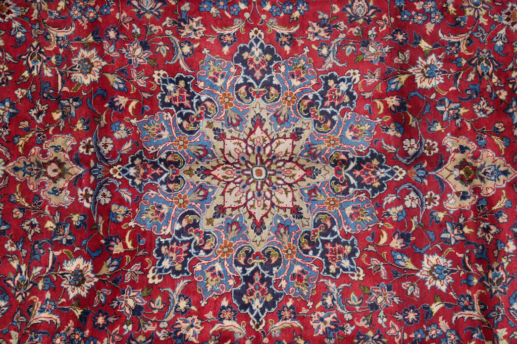A close-up of a traditional Persian-style rug with a vibrant red background and an intricate central medallion pattern in blue, beige, and cream.