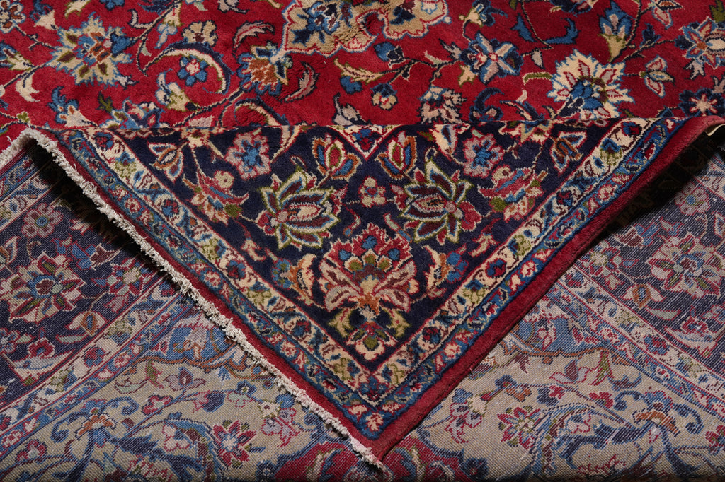 A close-up of an ornate patterned rug with a deep red field, dark navy central panel, and beige lower section, all decorated with intricate floral and vine motifs in blue, cream, and rust tones.